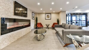 A modern lobby with a brick wall, a flat-screen TV, a glass coffee table, and a gray sofa.
