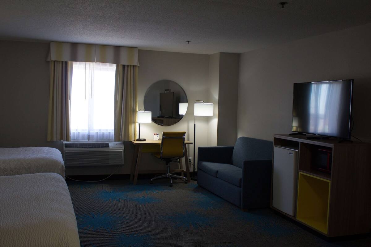 A hotel room with two beds, a desk with a chair, a television, and a minibar.