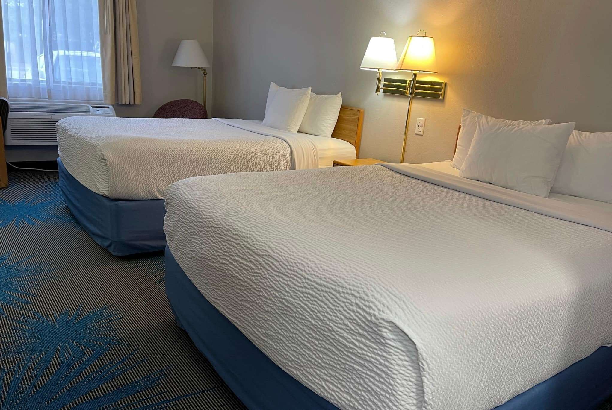 A hotel room with two beds, a desk, and a lamp.