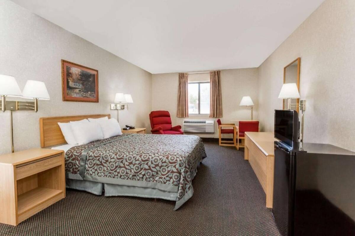 A hotel room with a bed, desk, chair, TV, and a painting on the wall.