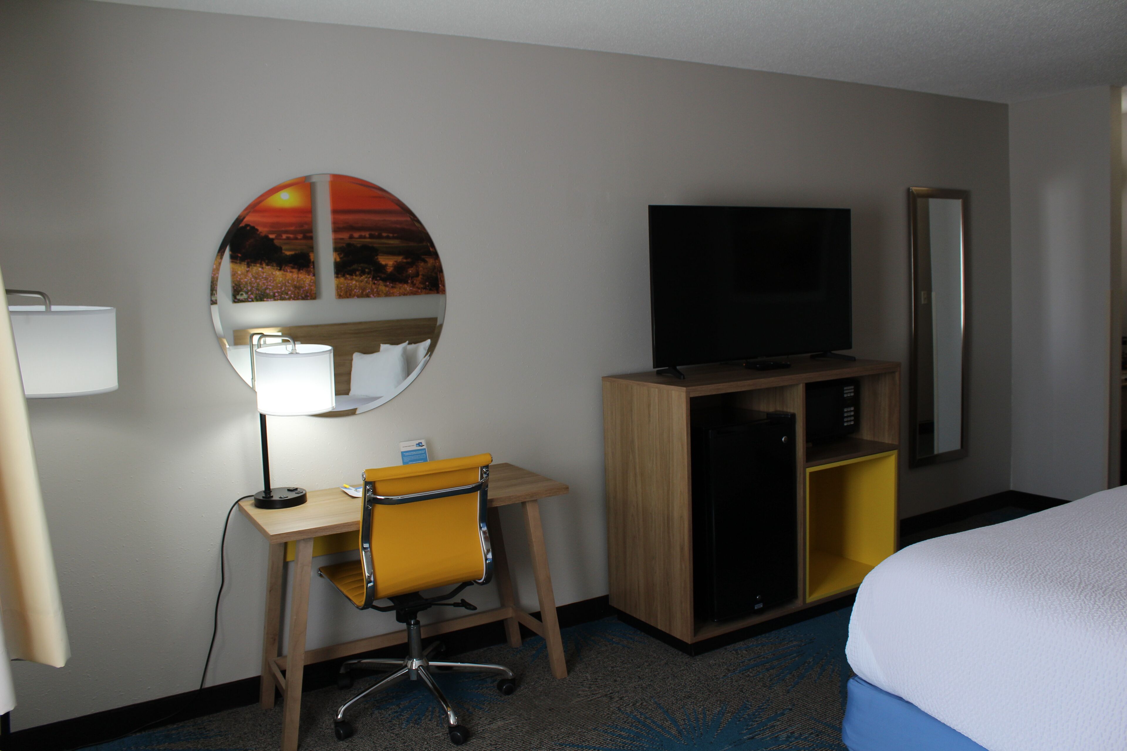 Hotelkamer met een bed, een bureau met stoel, een televisie, een spiegel en een wanddecoratie.