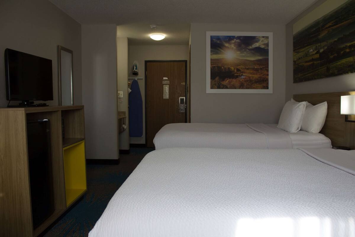 A hotel room with two beds, a TV, and a painting on the wall.