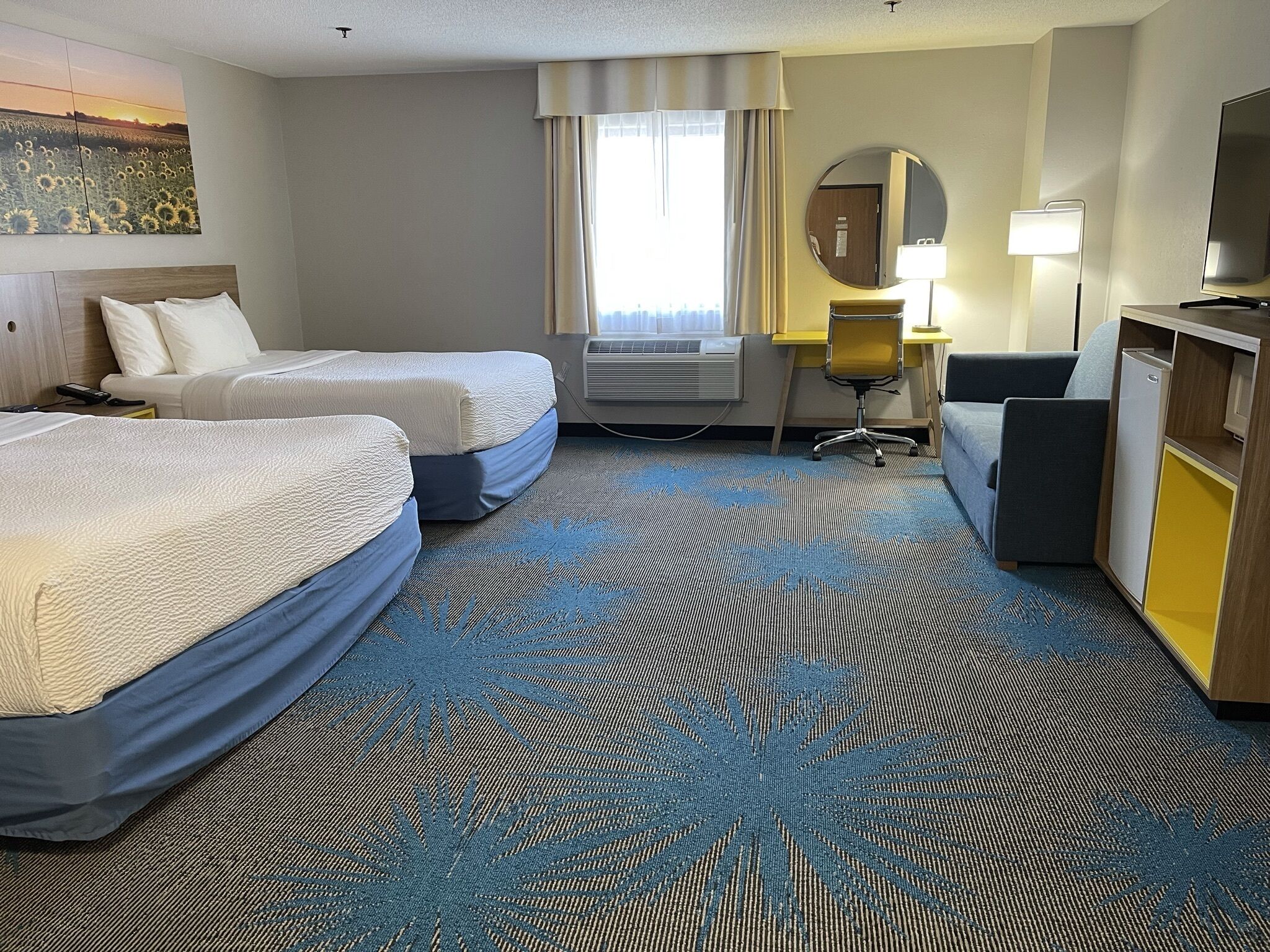 Una habitación de hotel con dos camas, un escritorio, una silla, un televisor y un ventanal con cortinas.