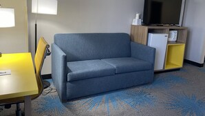 A hotel room with a grey sofa, a yellow table, a floor lamp, a TV, a mini-fridge, and a microwave. - Days Inn by Wyndham Colby (Colby)
