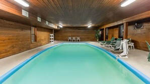 An indoor swimming pool with wooden walls and ceiling, surrounded by green lounge chairs and exercise equipment. - Days Inn by Wyndham Colby (Colby)