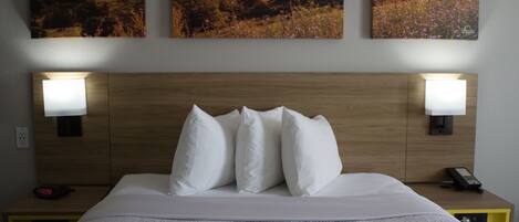 A neatly made bed with white linens and pillows, two bedside lamps, a bedside phone, and a nightstand with a clock.