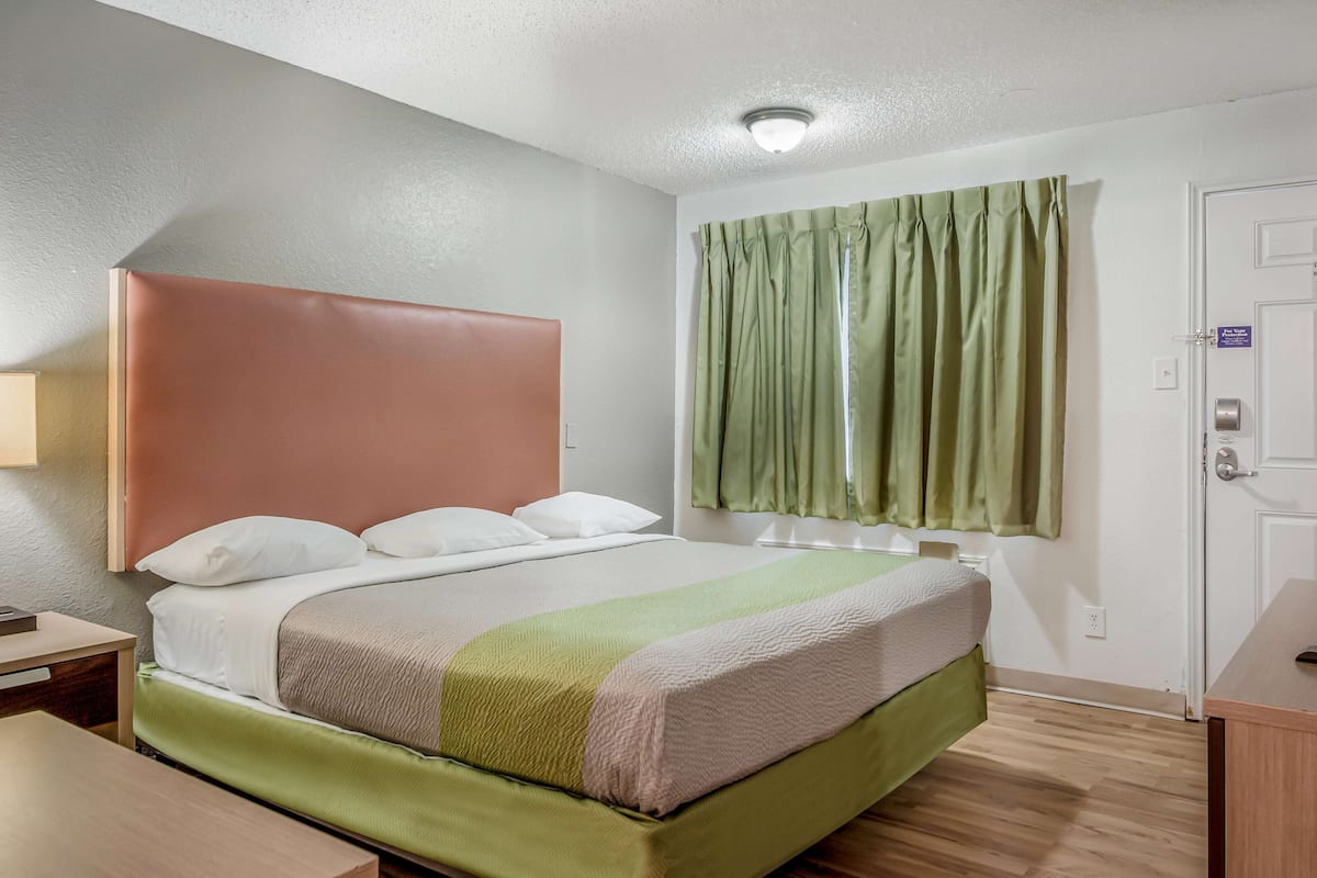 Ein Hotelzimmer mit Bett, Nachttisch, Schreibtisch, Fenster mit Vorhängen und einer Tür.