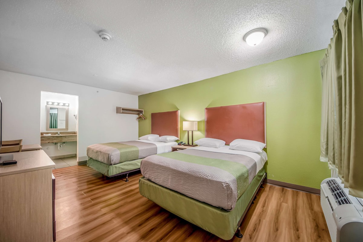 Ein Hotelzimmer mit zwei Betten, einem Schreibtisch, einem Spiegel, einem Schminktisch und einem Fenster.