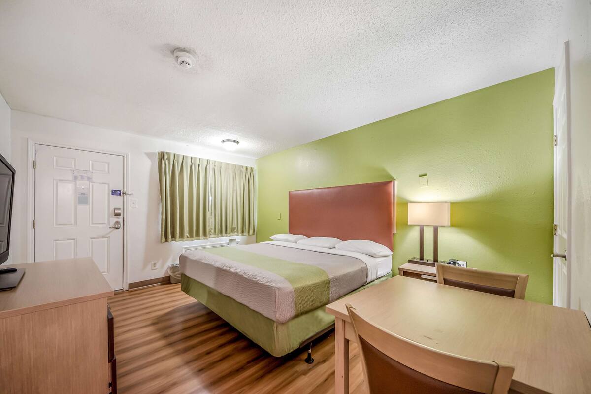 Ein Hotelzimmer mit einem Bett, einem Schreibtisch, einem Stuhl, einer Lampe und einem Fernseher.