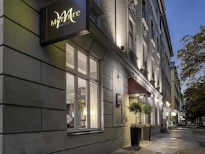 A hotel exterior with a sign reading 'Mure Hotels,' large windows, and potted plants. - Mercure Hotel Muenchen am Olympiapark (Munich)