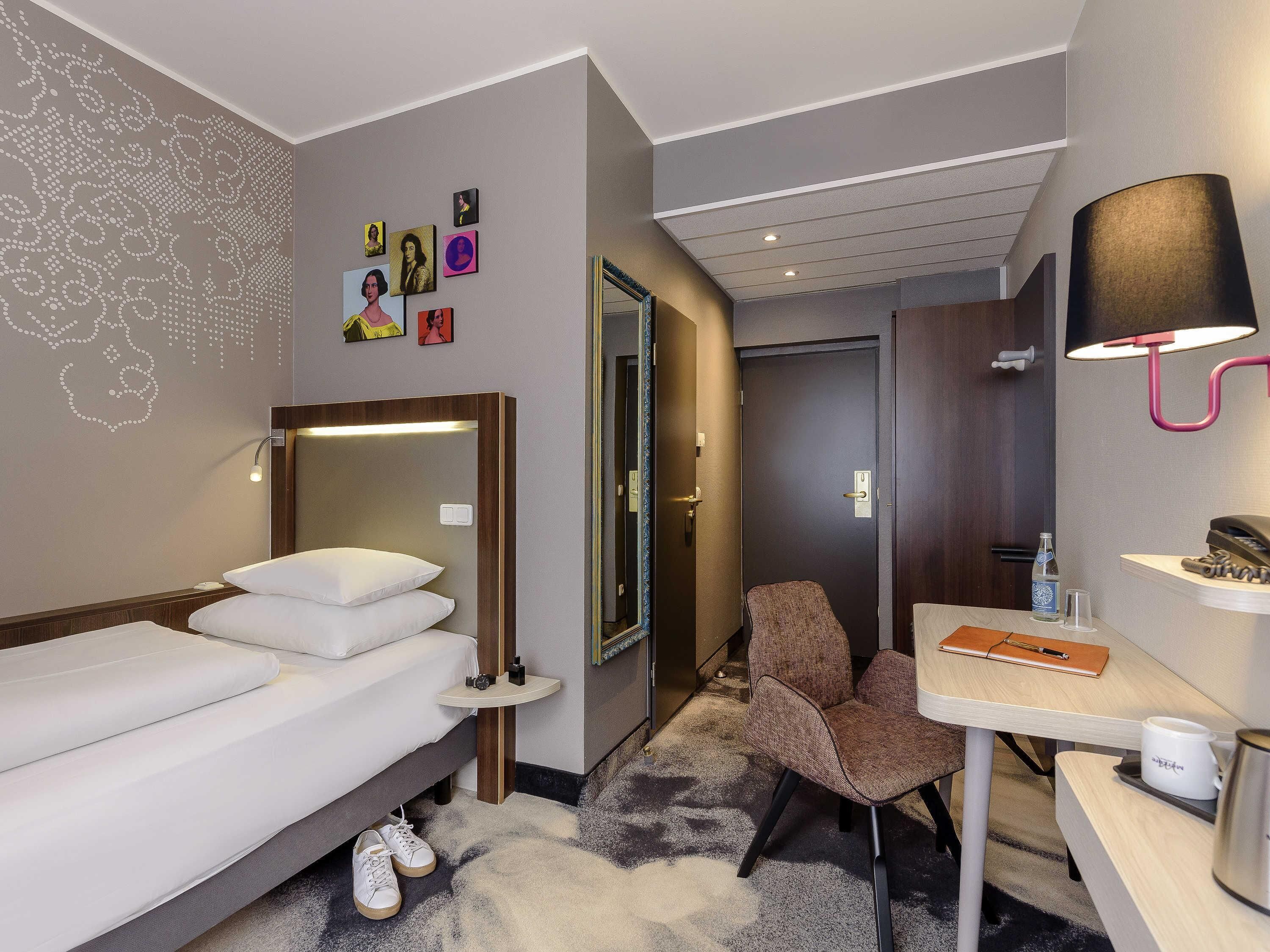 Una habitación de hotel con cama, escritorio, silla, espejo y decoración en la pared.