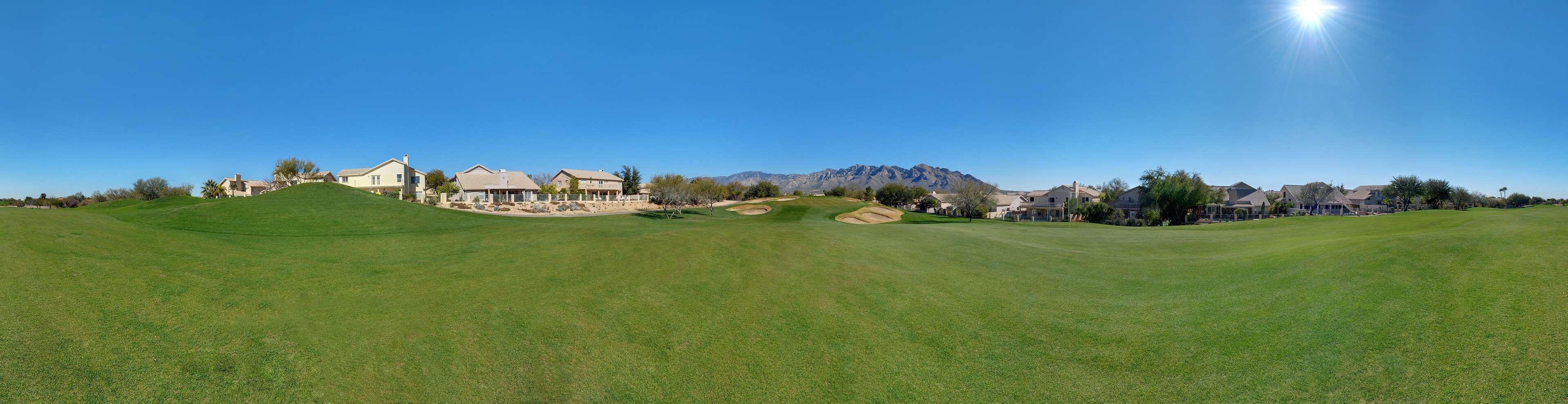 Un campo de golf con casas al fondo y montañas a lo lejos.
