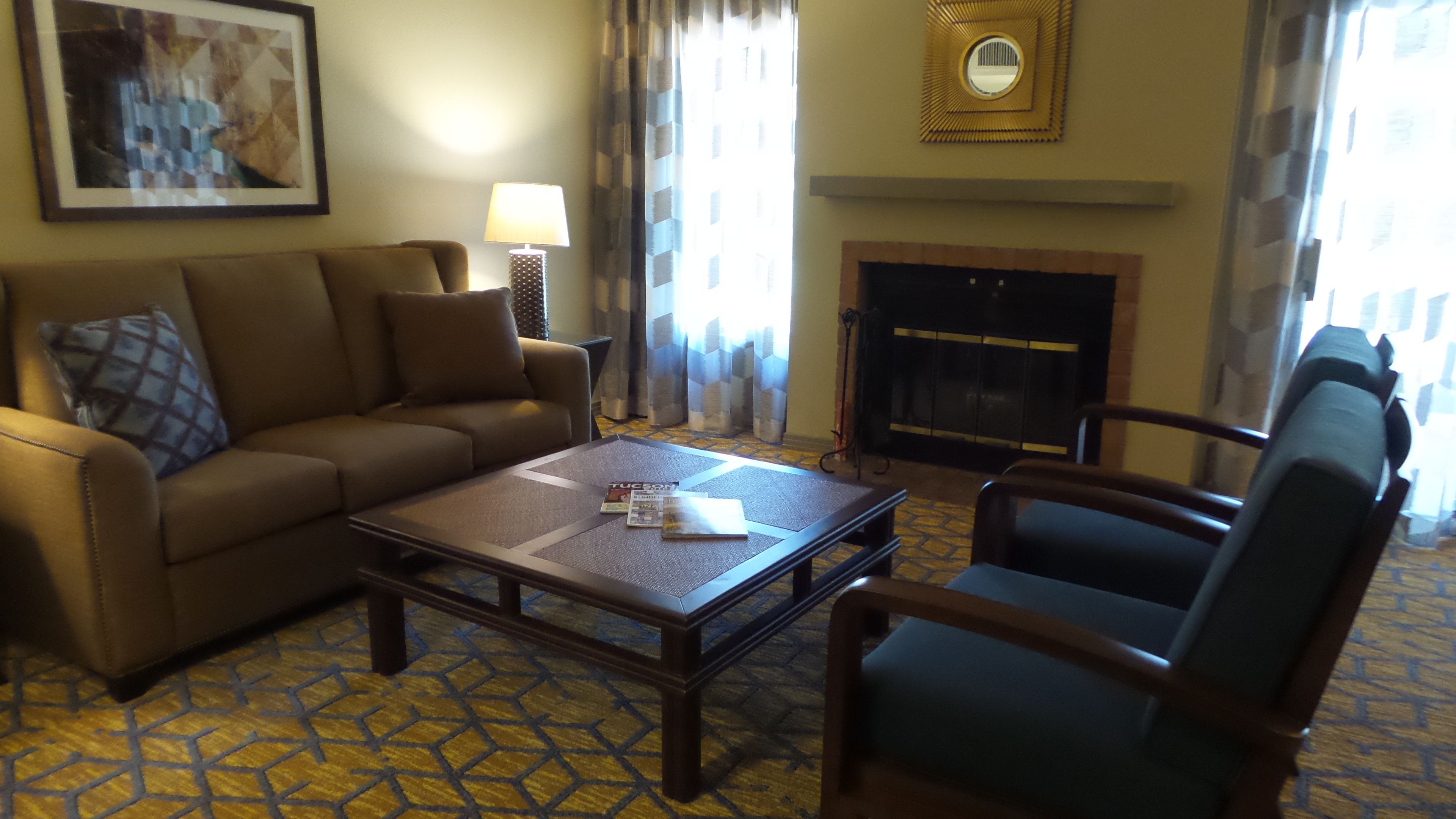 A living room with a sofa, armchair, coffee table, fireplace, and patterned carpet.