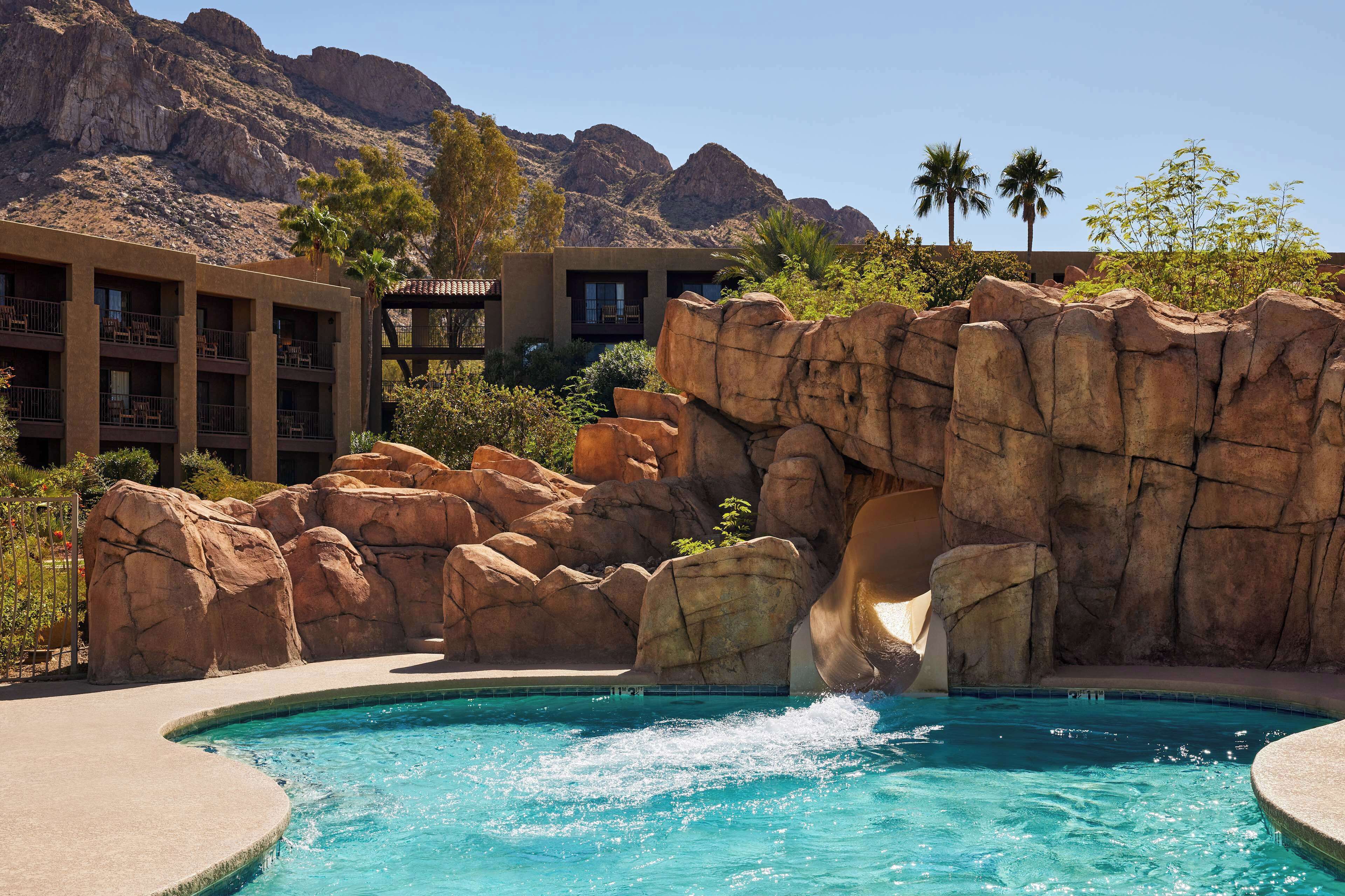 A pool with a rock waterfall, surrounded by a building with balconies and palm trees.