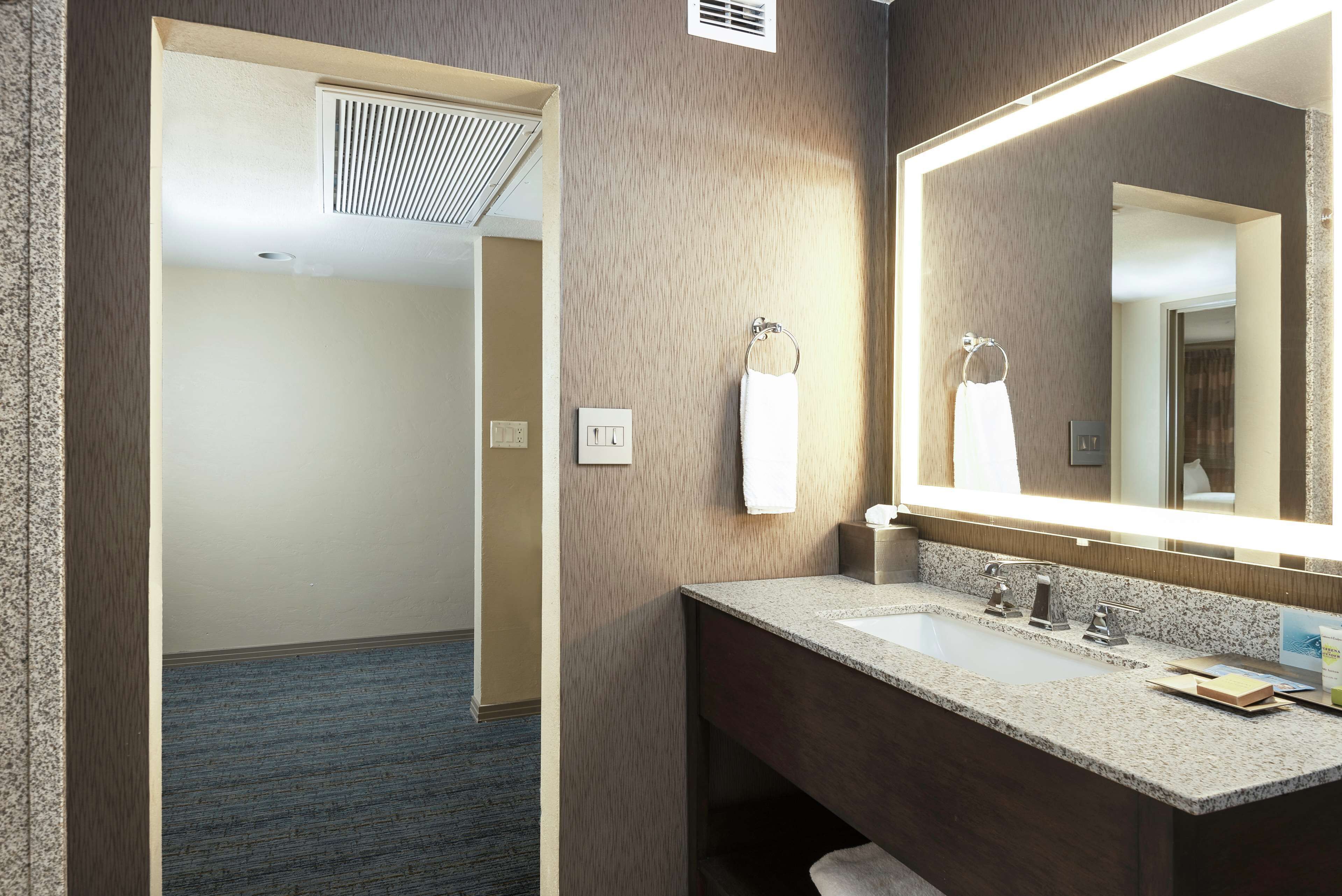 A hotel bathroom with a granite countertop sink, a large mirror, and a towel rack.