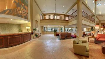 Um hall espaçoso com um balcão de recepção central, áreas de estar e um teto alto com murais decorativos.