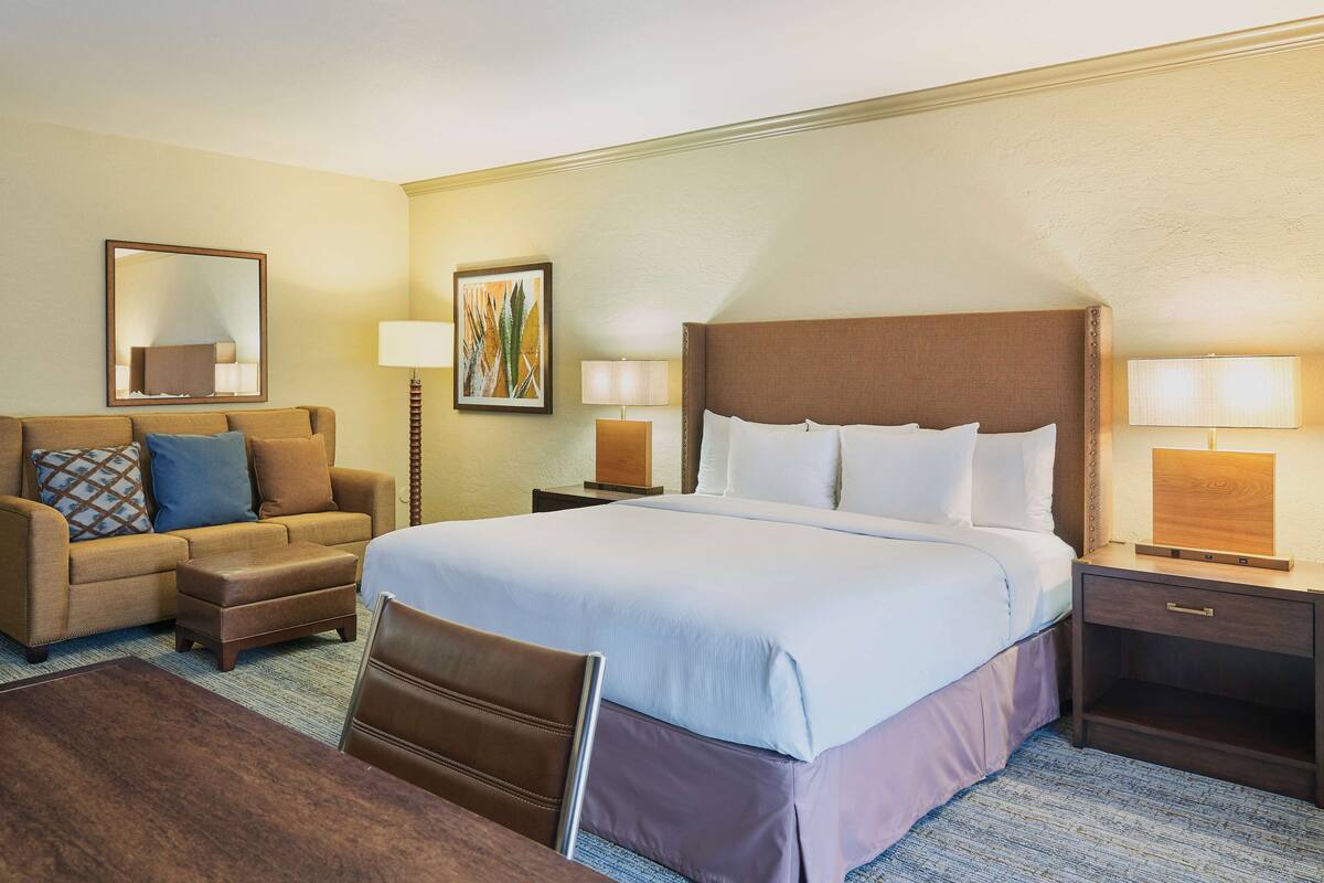 Una habitación de hotel con una cama grande, un sofá, un escritorio y dos lámparas.
