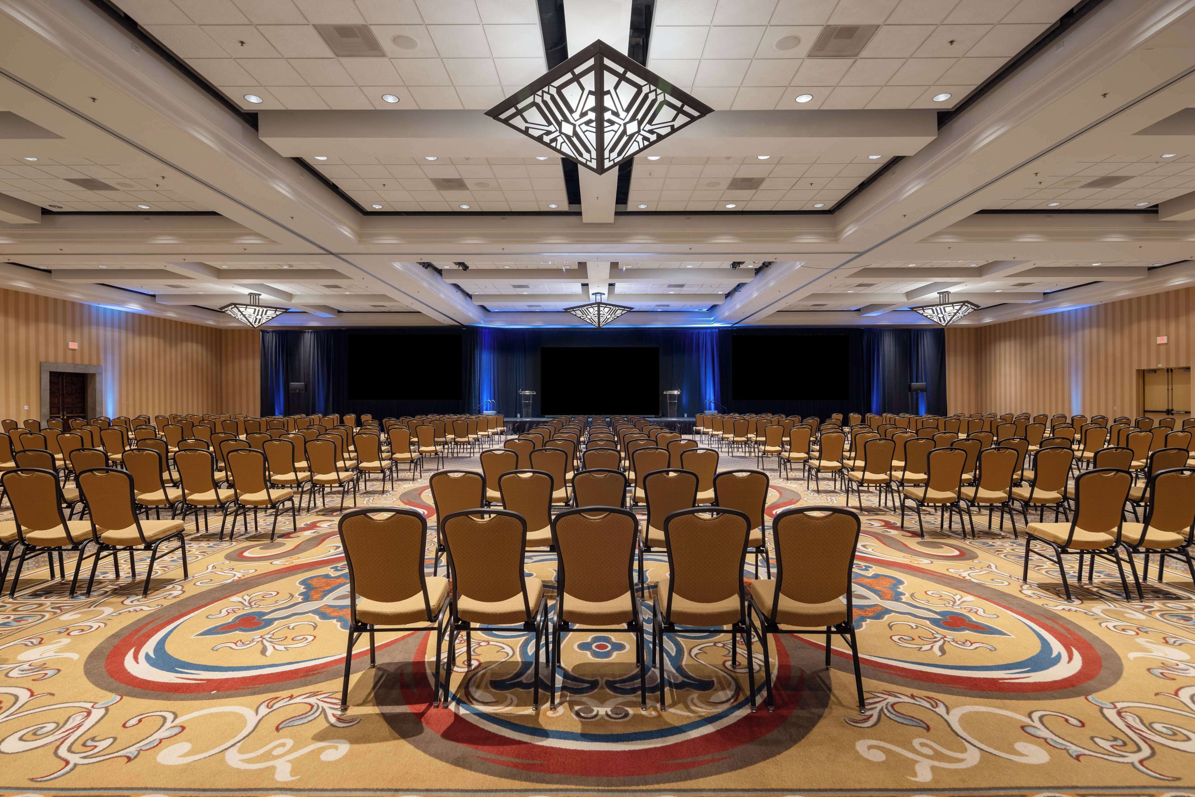A large conference room with rows of chairs, a patterned carpet, and a stage with curtains.