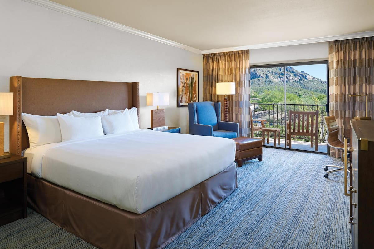 Habitación de hotel con una cama grande, una silla, un escritorio y un balcón con vistas a la montaña.