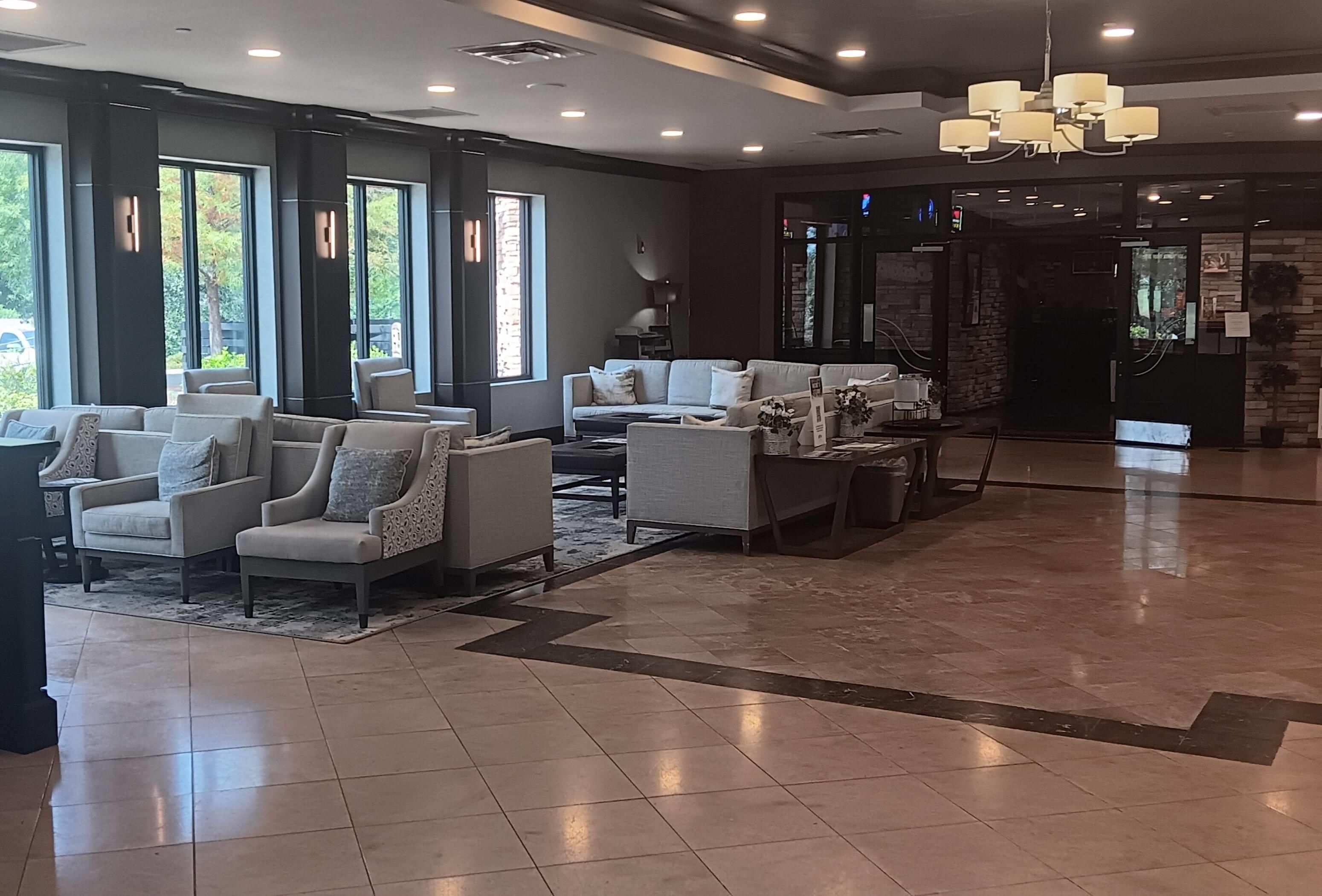 A modern lobby with a seating area, large windows, and a chandelier.