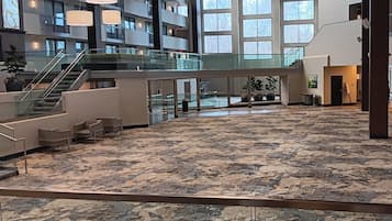 A spacious indoor area with a patterned carpet, a staircase, and a glass railing overlooking a lower level.
