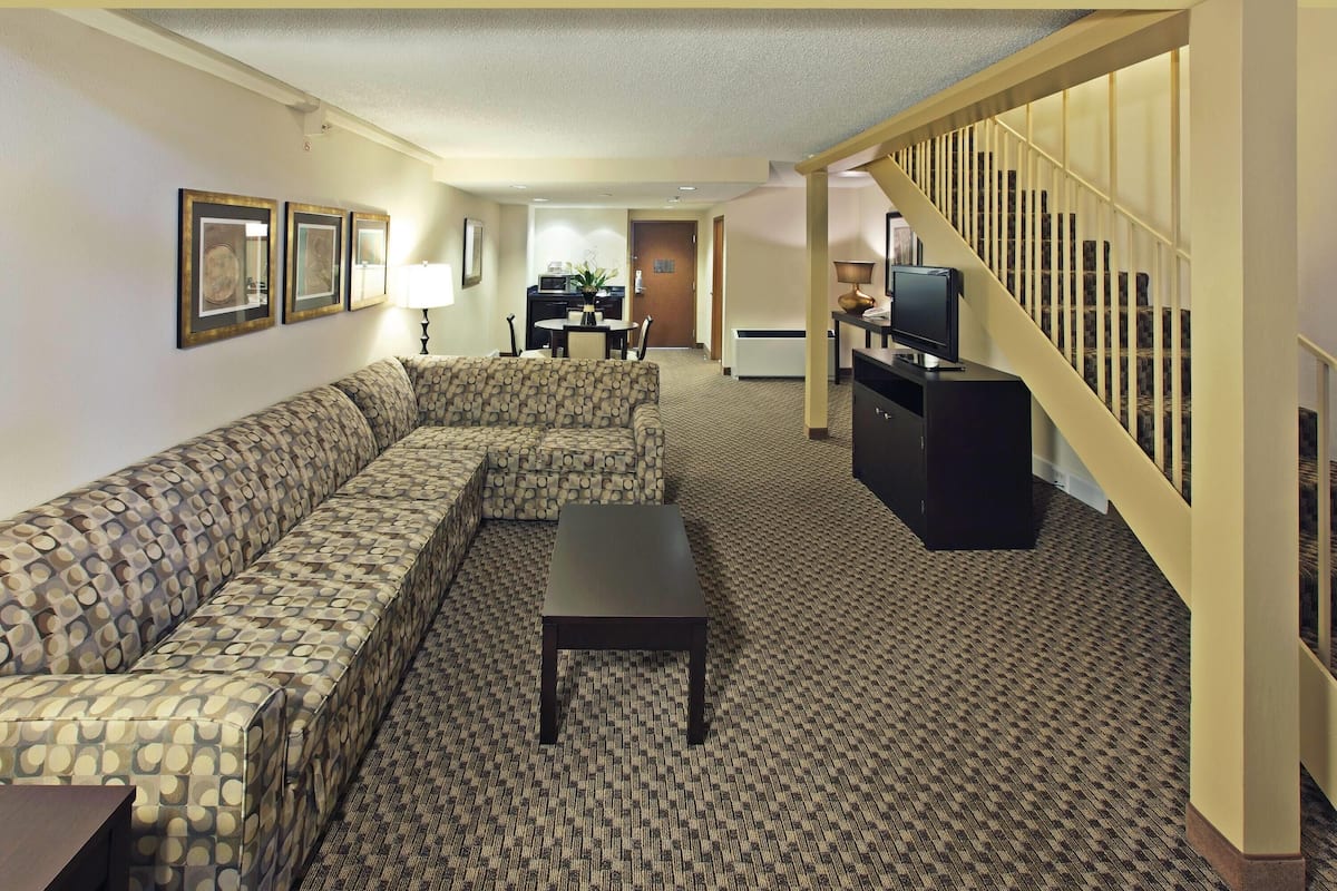 A hotel room with a patterned sofa, a small table, a TV, and a staircase.
