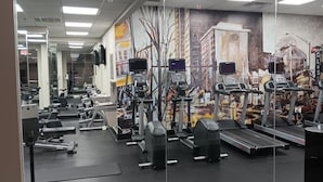 Un gimnasio con diferentes equipos de ejercicio, incluyendo cintas de correr y máquinas de pesas, y un mural en la pared.