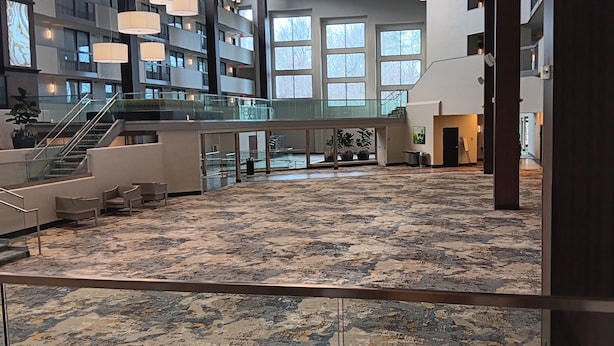 Un vestíbulo amplio con alfombra estampada, una escalera y una barandilla de vidrio que da a un nivel inferior.