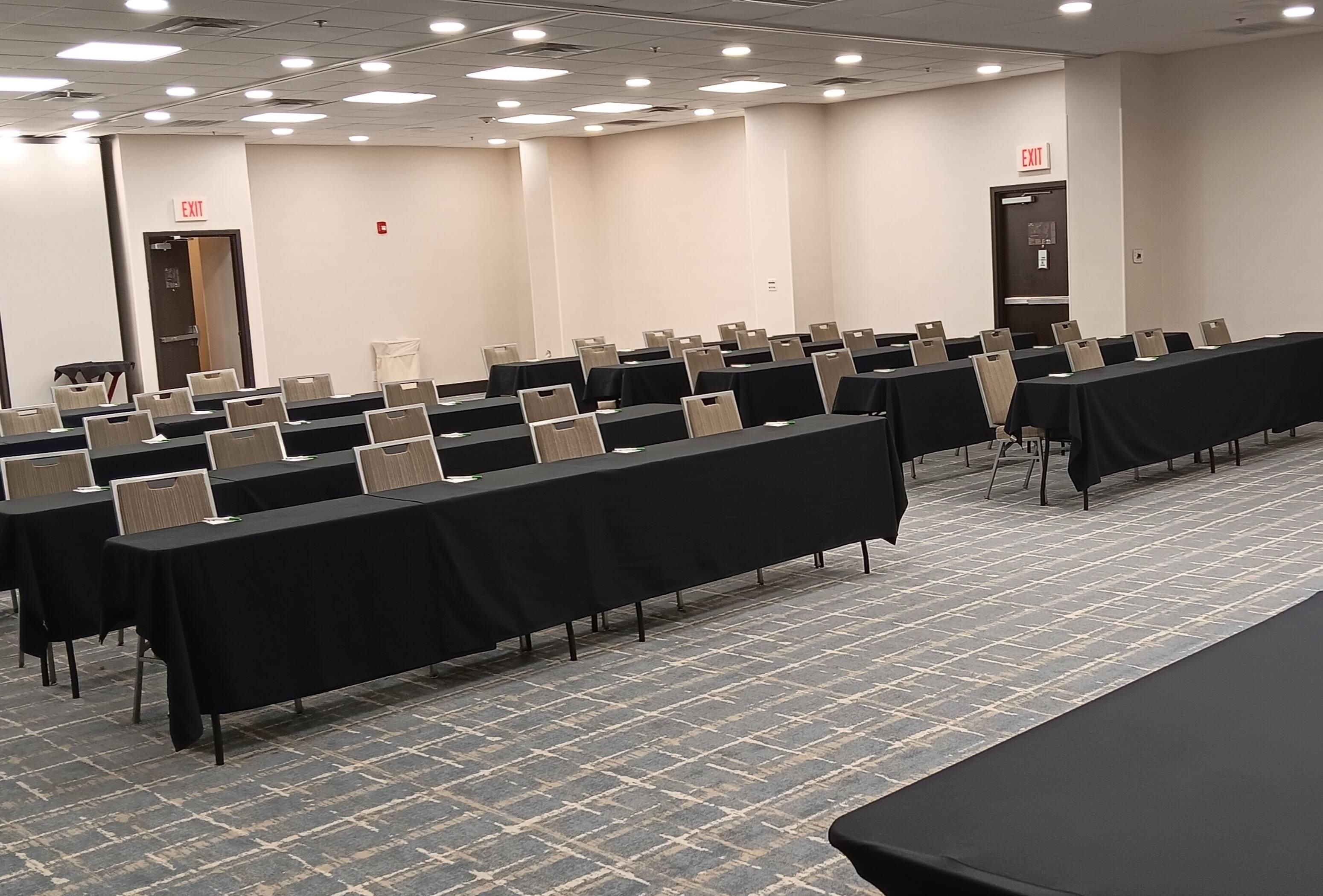 A conference room with rows of tables and chairs, exit signs on the walls, and a patterned carpet.