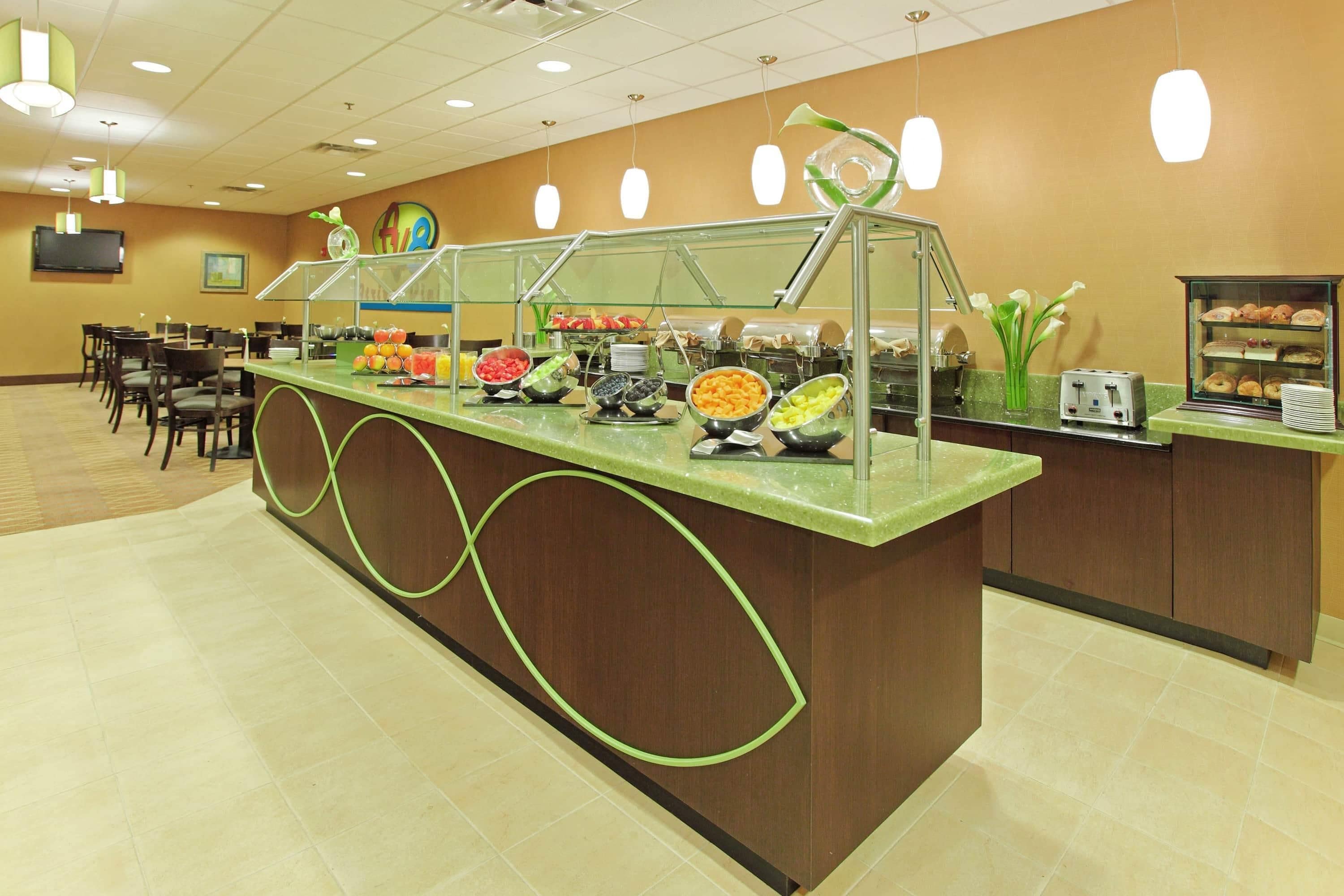 A buffet counter with various food items, a seating area with tables and chairs, and a television mounted on the wall.