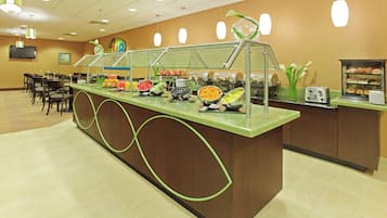 A buffet counter with various food items, a seating area with tables and chairs, and a television mounted on the wall.