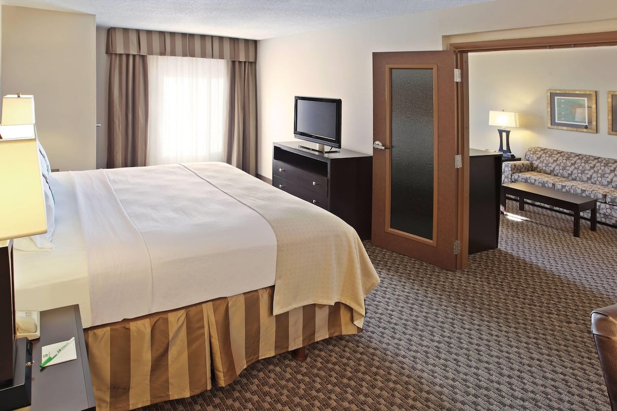 A hotel room with a bed, a television on a dresser, a sofa, and a door leading to another room.