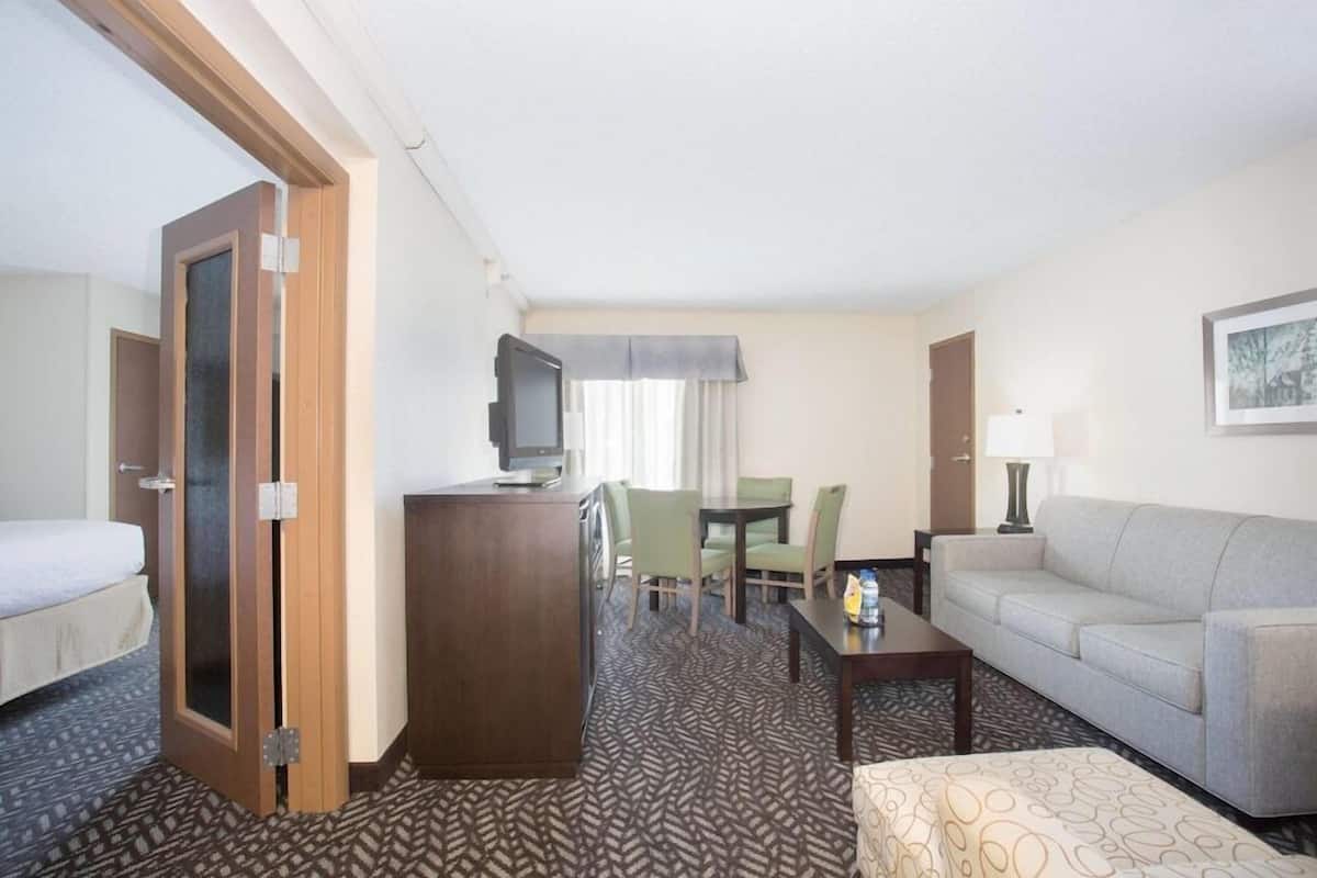 A hotel room with a bed, a desk, a TV, a sofa, and a dining table with chairs.