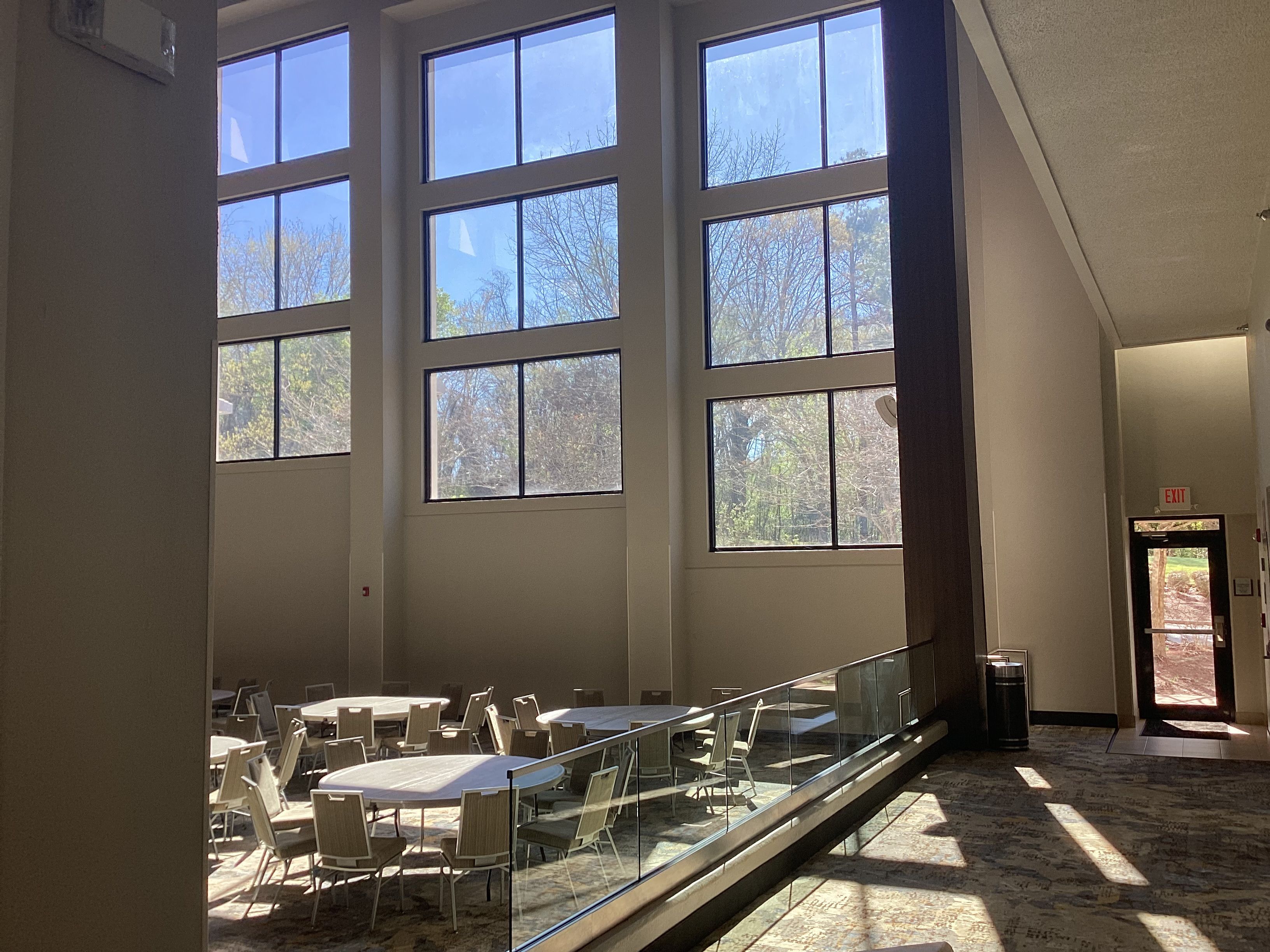 A spacious indoor area with large windows, a glass railing, and tables with chairs.