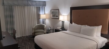 Habitación de hotel con una cama grande, una silla, una mesita de noche con lámpara y un cuadro colgado en la pared.