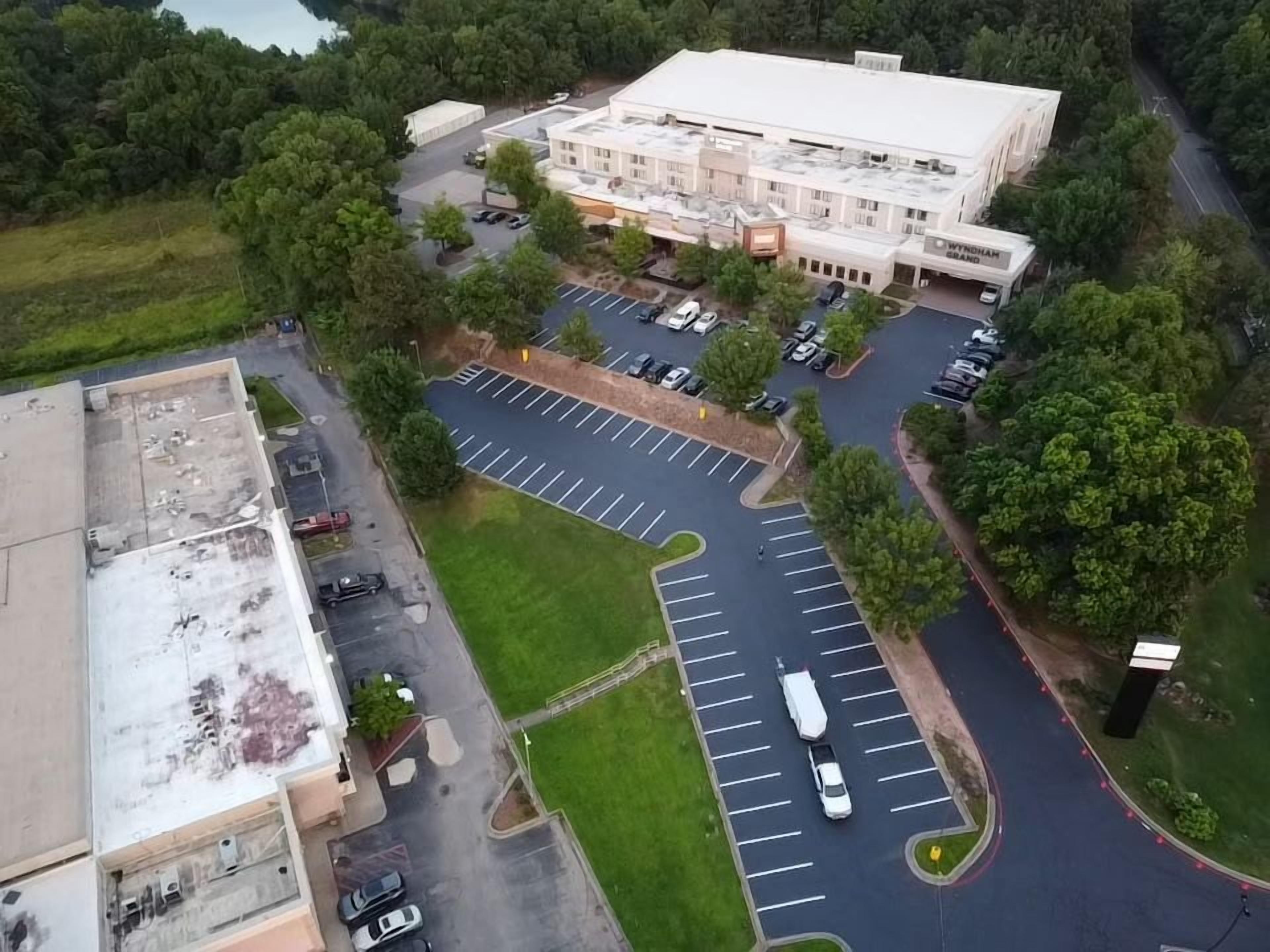 Vista aérea de un estacionamiento con múltiples filas de espacios, un edificio de techo plano y una carretera que serpentea alrededor del área.