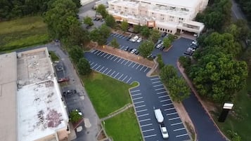 Vista aérea de un estacionamiento con múltiples filas de espacios, un edificio de techo plano y una carretera que serpentea alrededor del área.