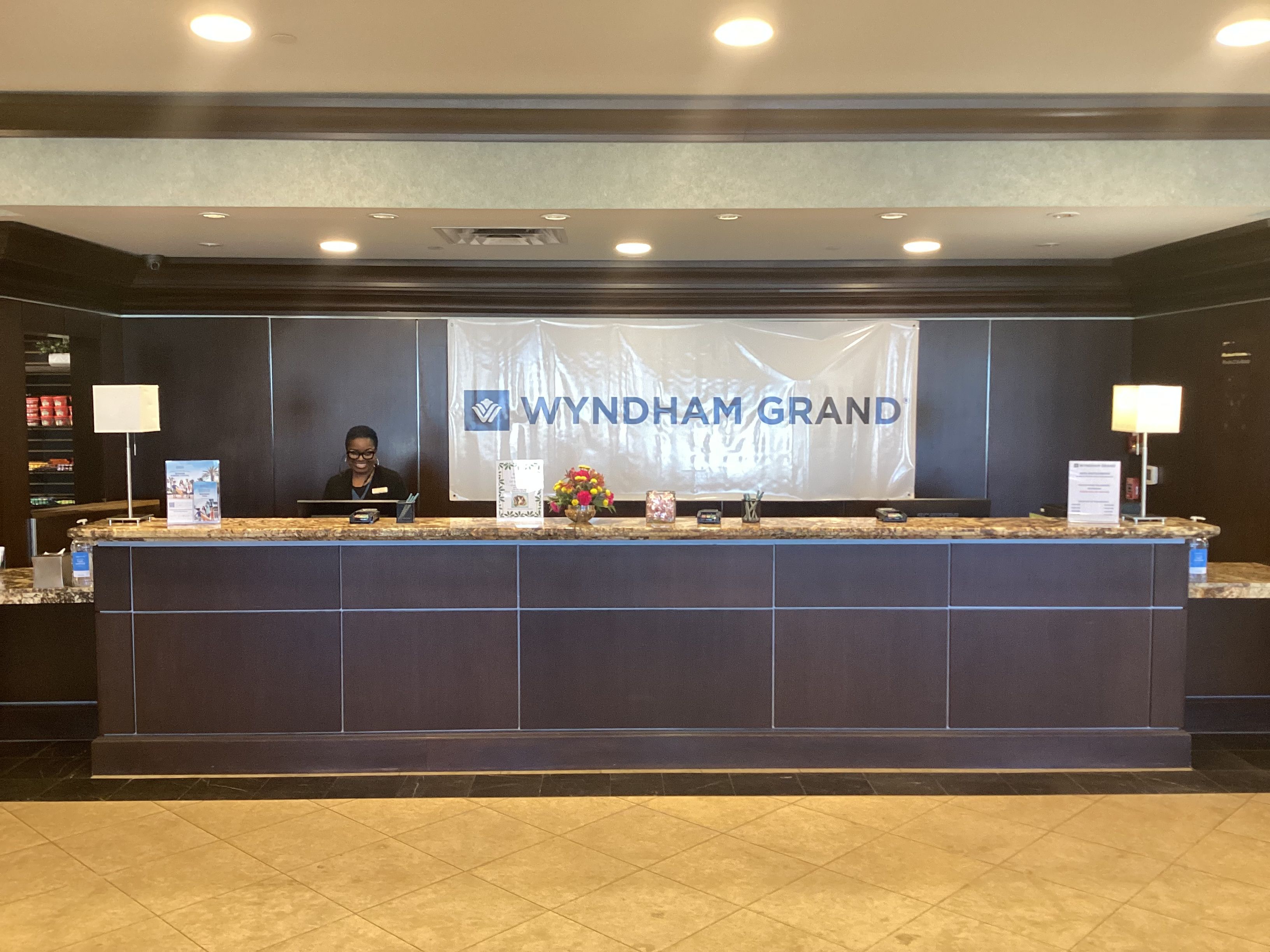 Una reception con uno striscione che riporta 'WYNDHAM GRAND' e un addetto alla reception dietro al bancone.
