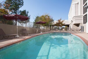 A swimming pool with lounge chairs and umbrellas, surrounded by a fence and trees.