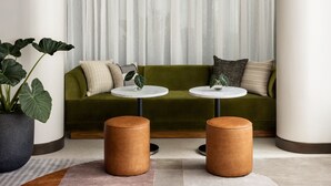 A modern living room with a green sofa, two round tables, a large potted plant, and a unique chandelier. - Kimpton Theta New York - Times Square by IHG (New York)