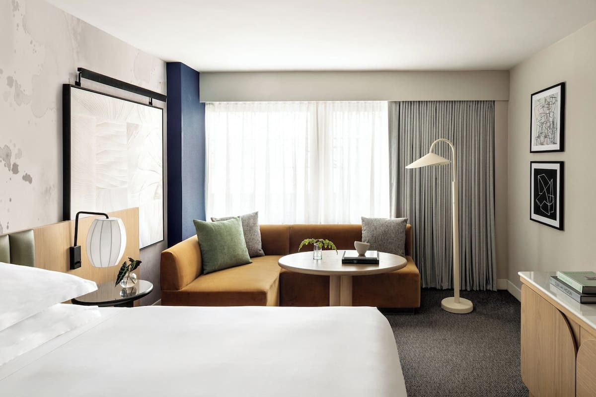 A modern hotel room with a bed, a sofa, a round table, and a desk.