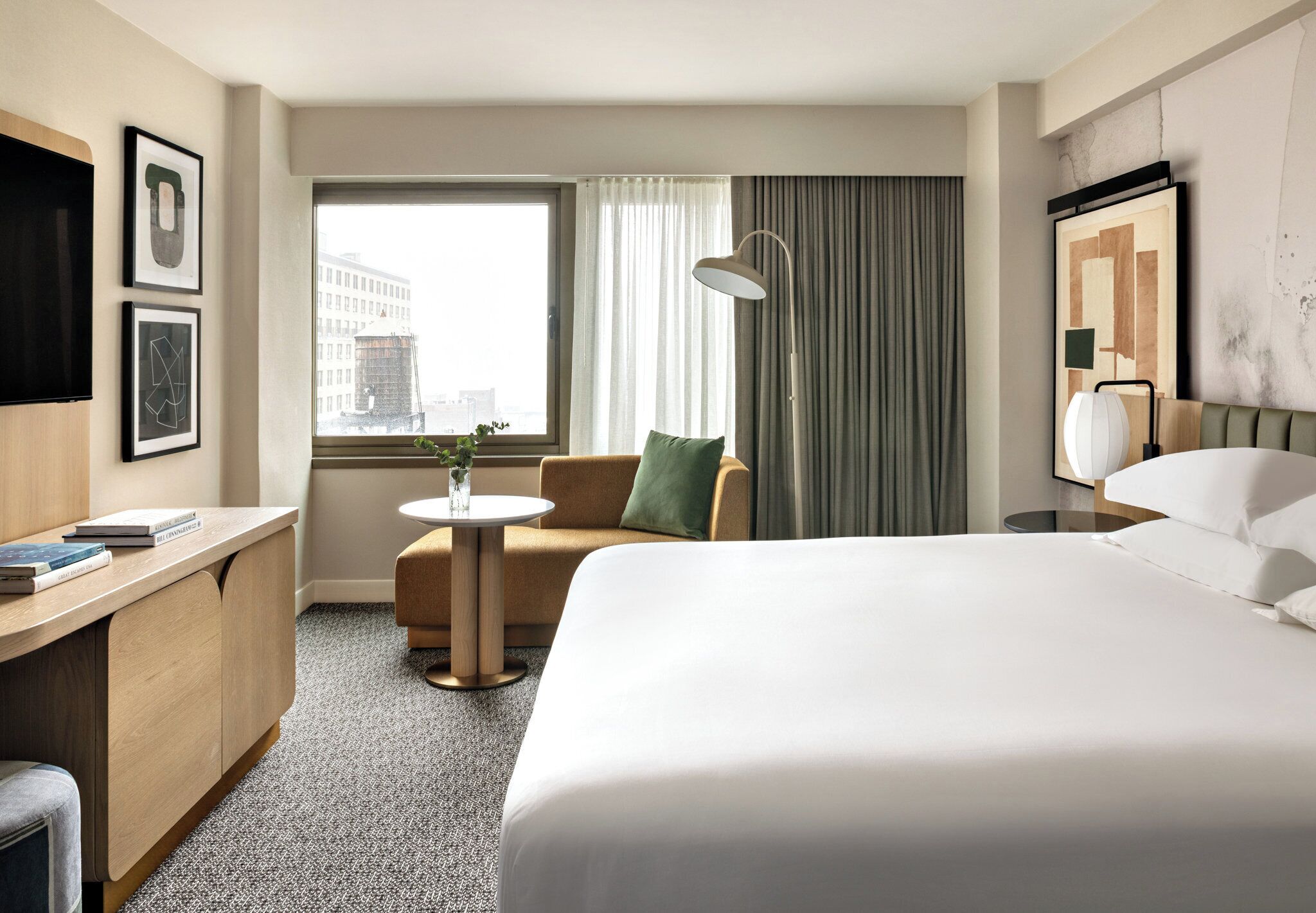 A hotel room with a large bed, a desk, a chair, a small table, and a window with curtains.