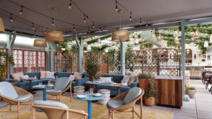 A modern outdoor seating area with wicker furniture, a bar, and a view of greenery. - Kimpton Theta New York - Times Square by IHG (New York)