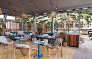 A modern outdoor seating area with wicker furniture, a bar, and a view of greenery. - Kimpton Theta New York - Times Square by IHG (New York)