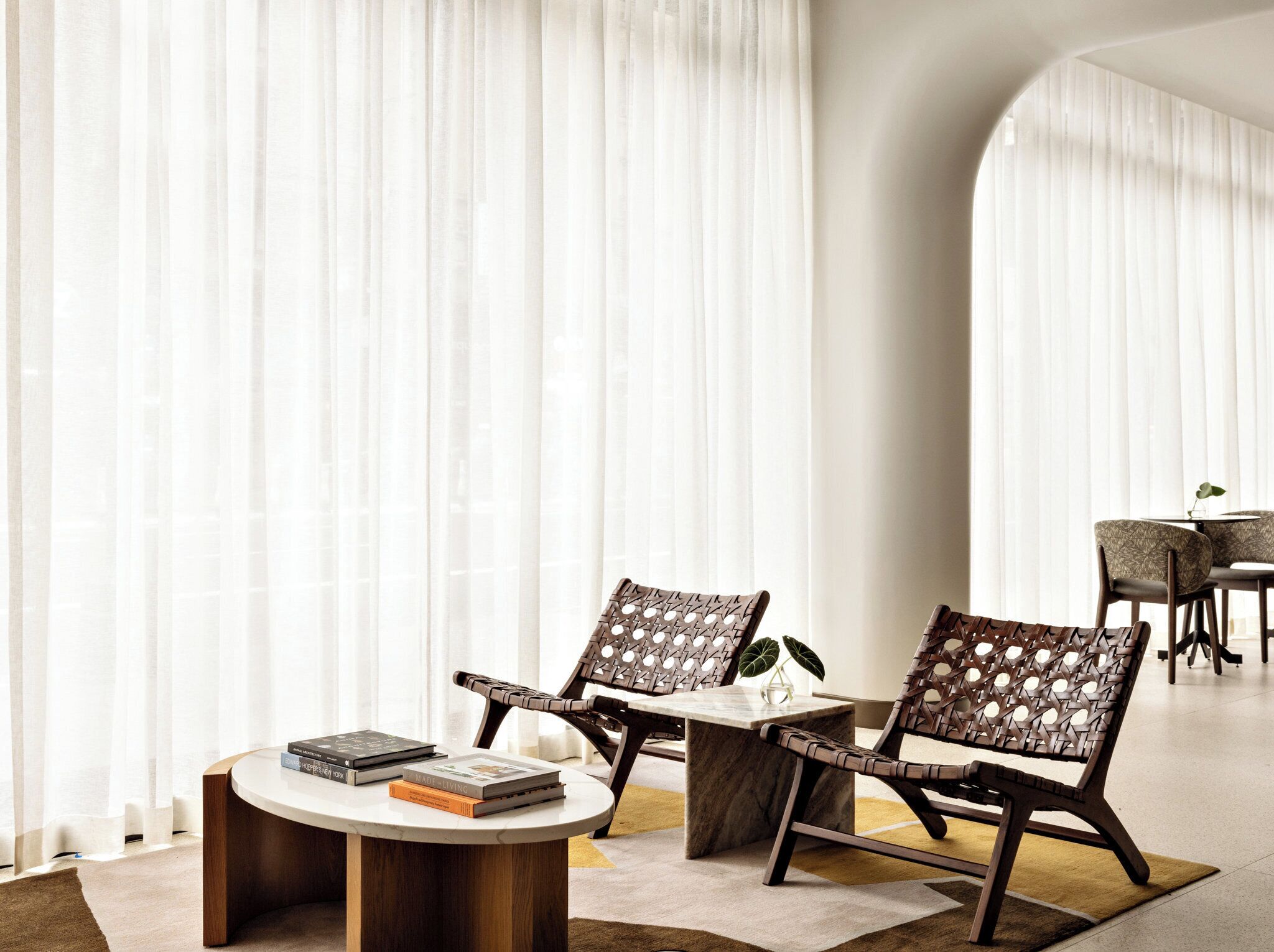 A modern interior with two wicker chairs, a round table, and books.