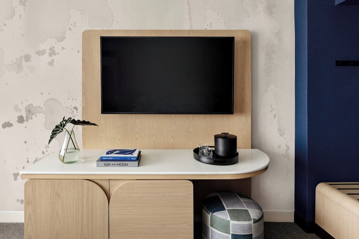 A modern room with a wooden desk, a mounted TV, a small plant, and a book titled "SUN and MOON".