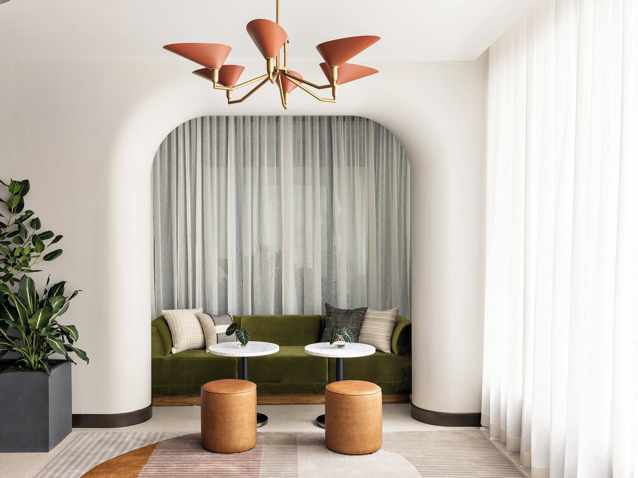 A modern living room with a green sofa, two round tables, a large plant, and a unique ceiling light fixture.