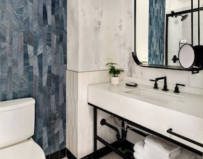A modern bathroom with a white sink, black faucet, and a mirror above it. There is a potted plant on the counter and a towel rack below the sink. - Kimpton Theta New York - Times Square by IHG (New York)