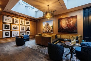 Un interior moderno con techo alto, tragaluces, una zona de estar con sofás y sillones, y una pared decorada con fotografías enmarcadas.