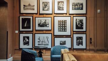 Una pared con fotografías blanco y negro enmarcadas, una mesa redonda con un libro y dos sillas azules.